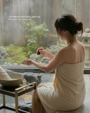 Woman in a towel applying oil by a hot spring with a garden view