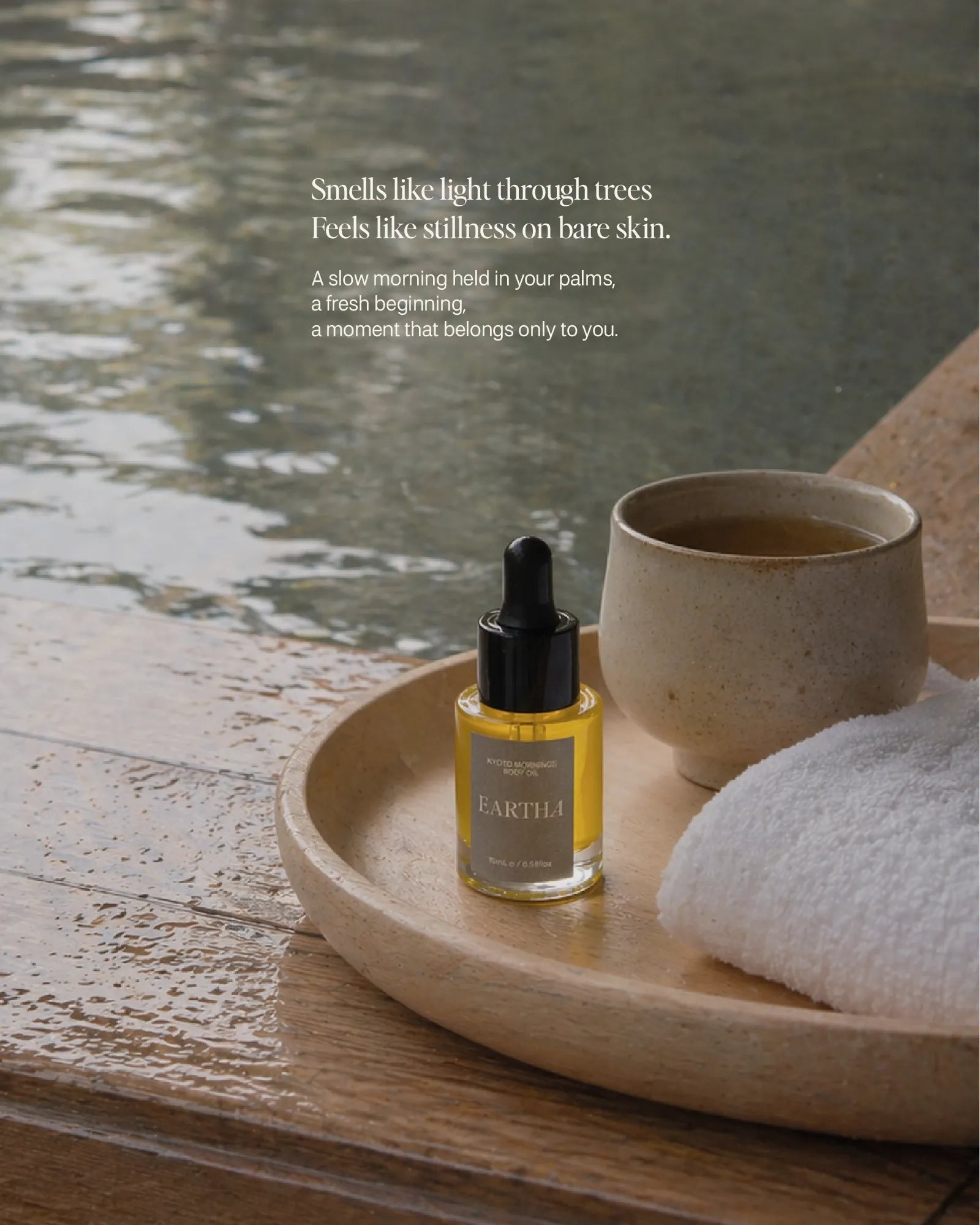 Bottle of Eartha Kyoto Mornings Body Oil by the hot spring with a warm cup of tea and towel