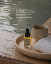 Bottle of Eartha Kyoto Mornings Body Oil by the hot spring with a warm cup of tea and towel