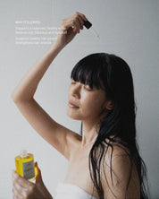 Woman with damp hair holding a dropper bottle and a bottle of scalp oil from Eartha against a plain background.