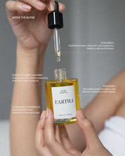 Hand holding a dropper over an Eartha scalp oil bottle with text on a gray background
