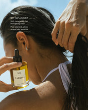Woman holding a bottle of Eartha hair product with another hand touching their hair.