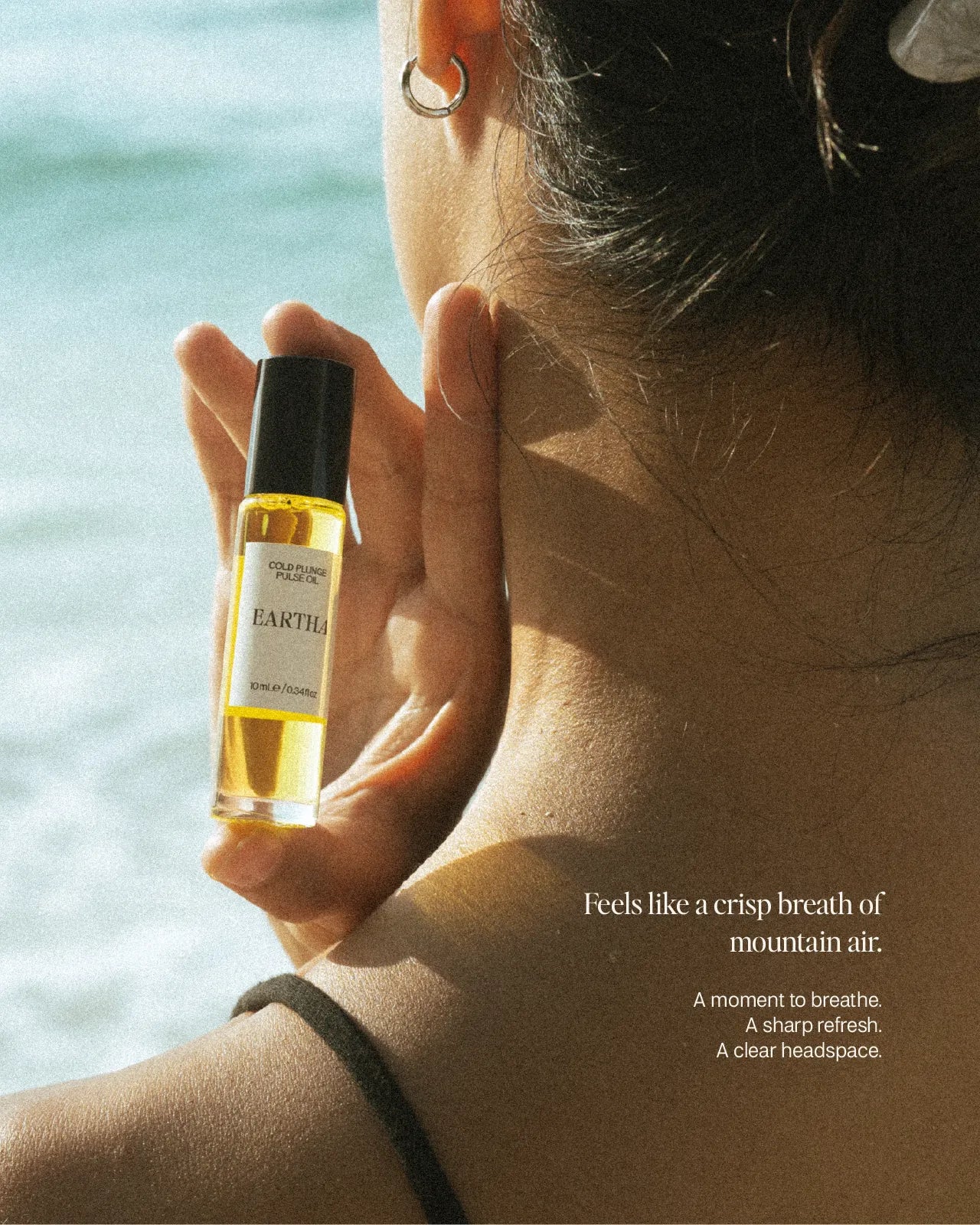 Woman holding a bottle of Eartha essential oil roll-on with a scenic background