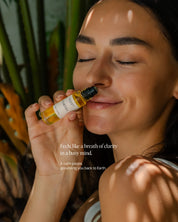Woman holding a bottle of Quiet Moments essential oil roll-on with nature in the background