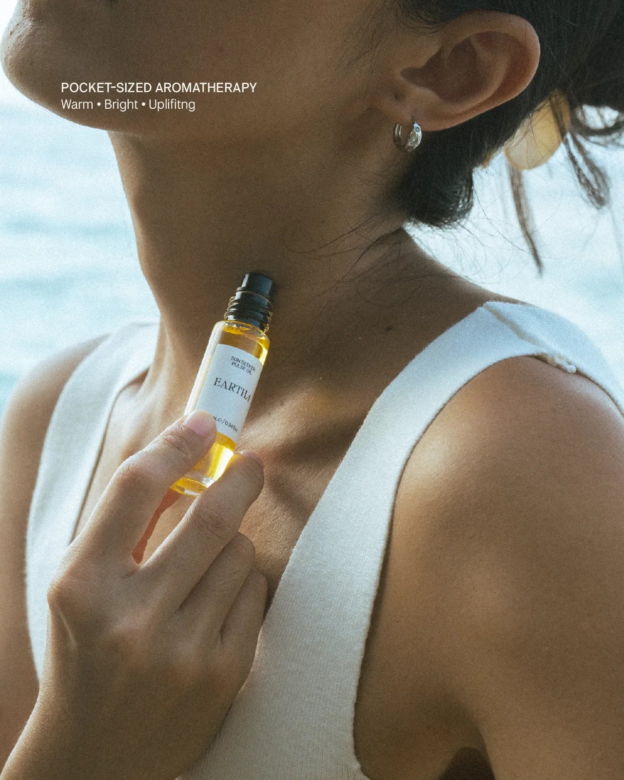 Woman holding a small bottle of Eartha Sun Seeker essential oil roll-on at the beach