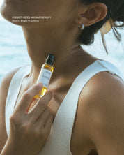 Woman holding a small bottle of Eartha Sun Seeker essential oil roll-on at the beach