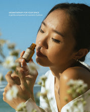 Woman smelling a bottle of essential oil with flowers and blue sky in the background