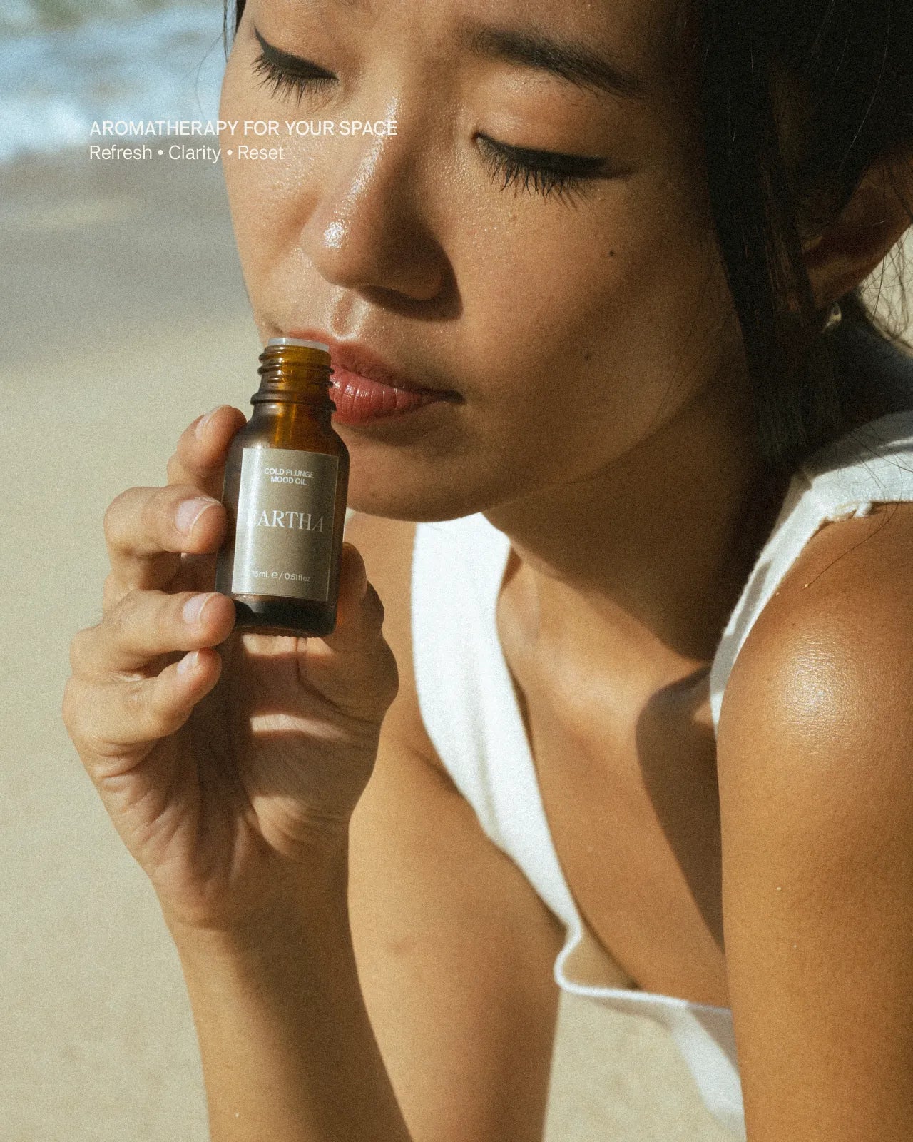 Woman holding a bottle of Eartha essential oil at the beach