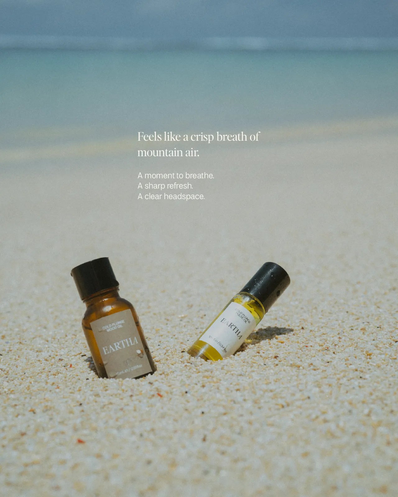Two bottles of Cold Plunge essential oil and roll-on on a sandy beach with a scenic background