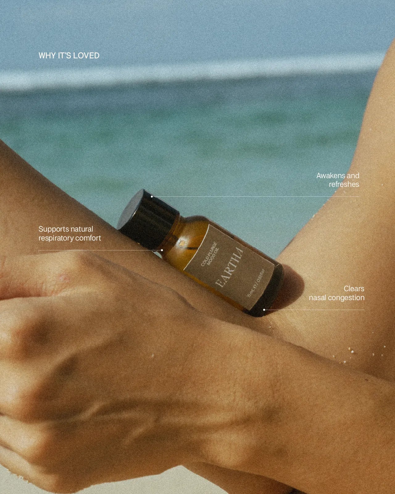 Hand holding a bottle of Eartha essential oil with ocean in the background