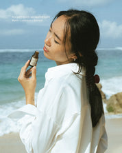 Woman holding a bottle of essential oil on a beach with ocean and sky in the background