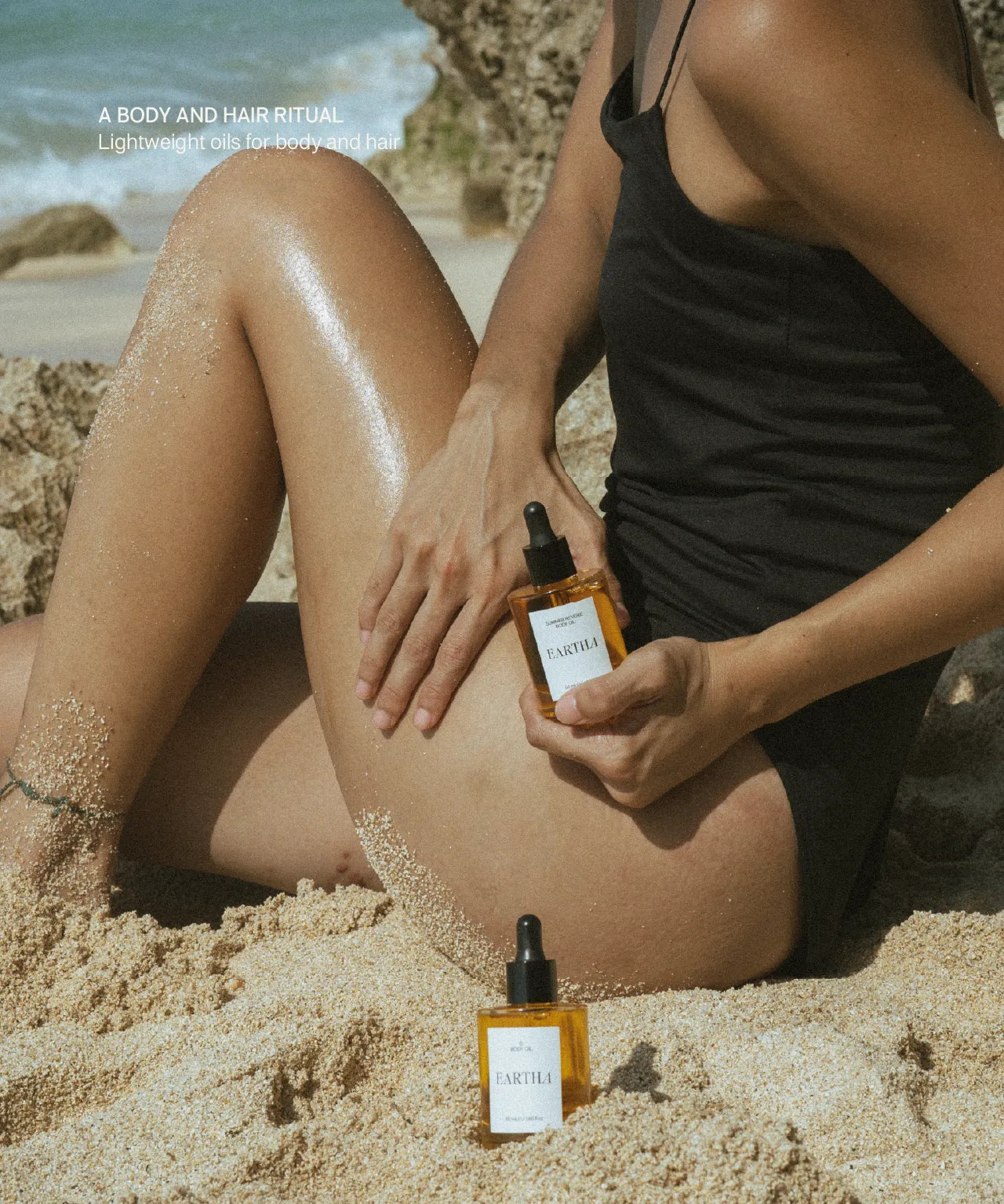 Person on a beach holding a bottle of 'Eartha' product with another bottle on the sand.