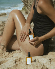Person on a beach holding a bottle of 'Eartha' product with another bottle on the sand.